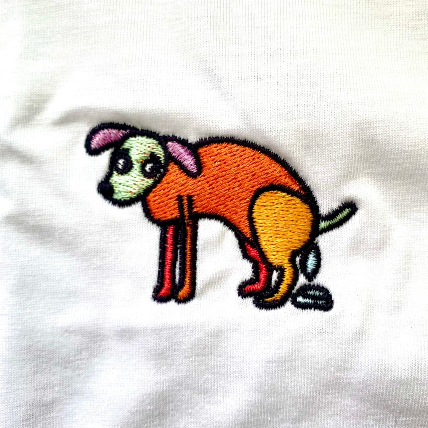 Shirt met borduurwerk van tekening van poepende hond door Anne Neuteboom cabaretier in Anne Neut Boetiek